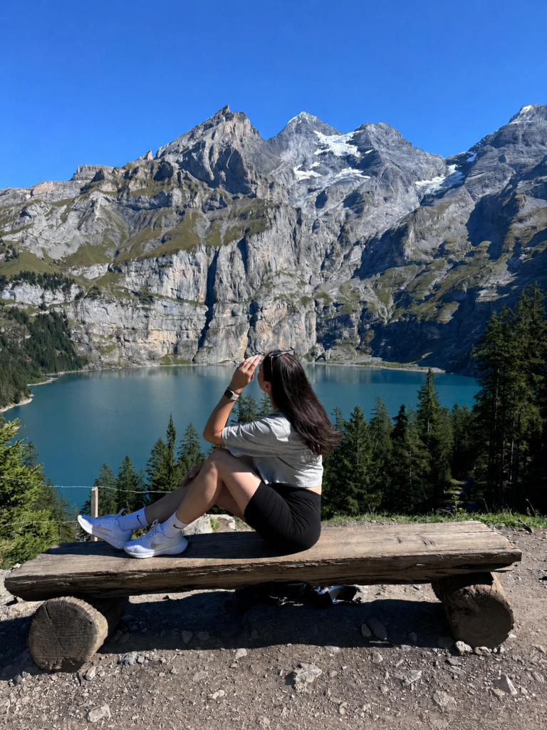 Woman sitting on a wooden bench overlooking Oeschinensee and the Swiss Alps